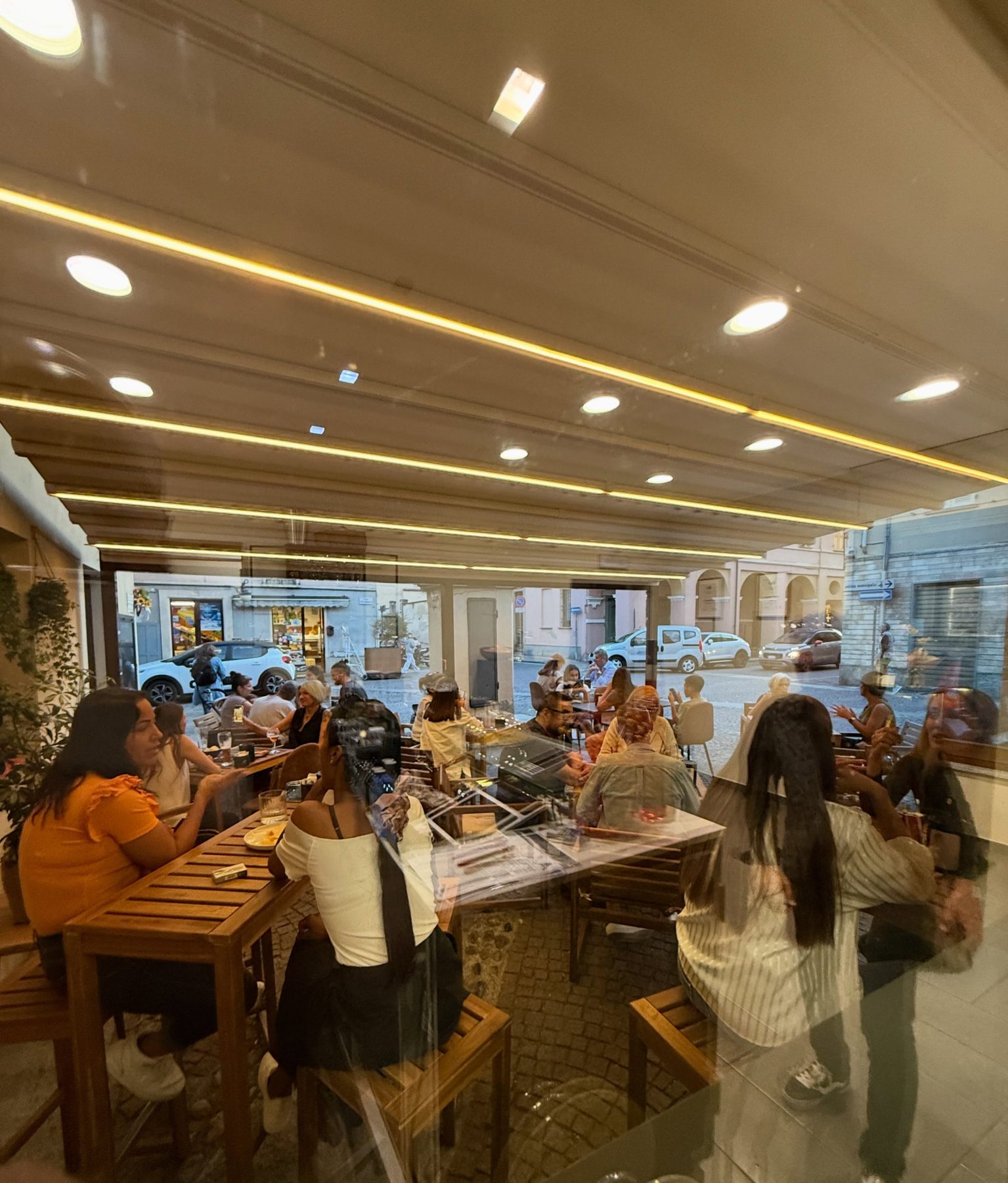 Il dehors di Civico.9 la sera, con i tavoli in legno pieni e la piazza sullo sfondo